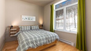 A bedroom with a bed, a window with curtains, a wall-mounted shelf, and a framed picture. - Le Méridien 33: Spa, River Views, Near Le Massif (Petite-Rivière-Saint-François)