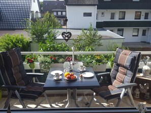 Un balcon avec une table dressée pour deux personnes, des chaises et des plantes en pot.