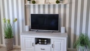A living room with a TV on a white cabinet, striped wallpaper, and potted plants. - Watt's Happiness Close to the Beach (Büsum)