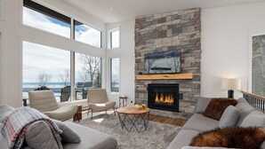A modern living room with a stone fireplace, large windows, and a cozy seating area.