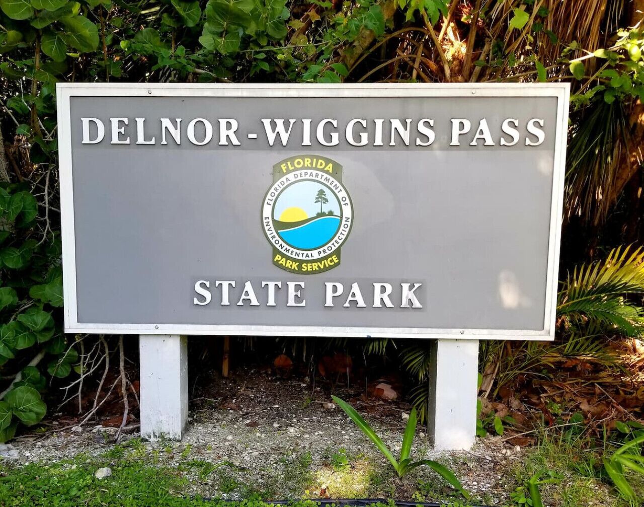 A sign for Delnor-Wiggins Pass State Park with the Florida Department of Environmental Protection logo.