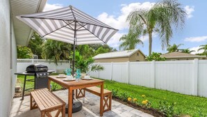Une terrasse avec une table et des bancs en bois, un barbecue et un parasol à rayures.