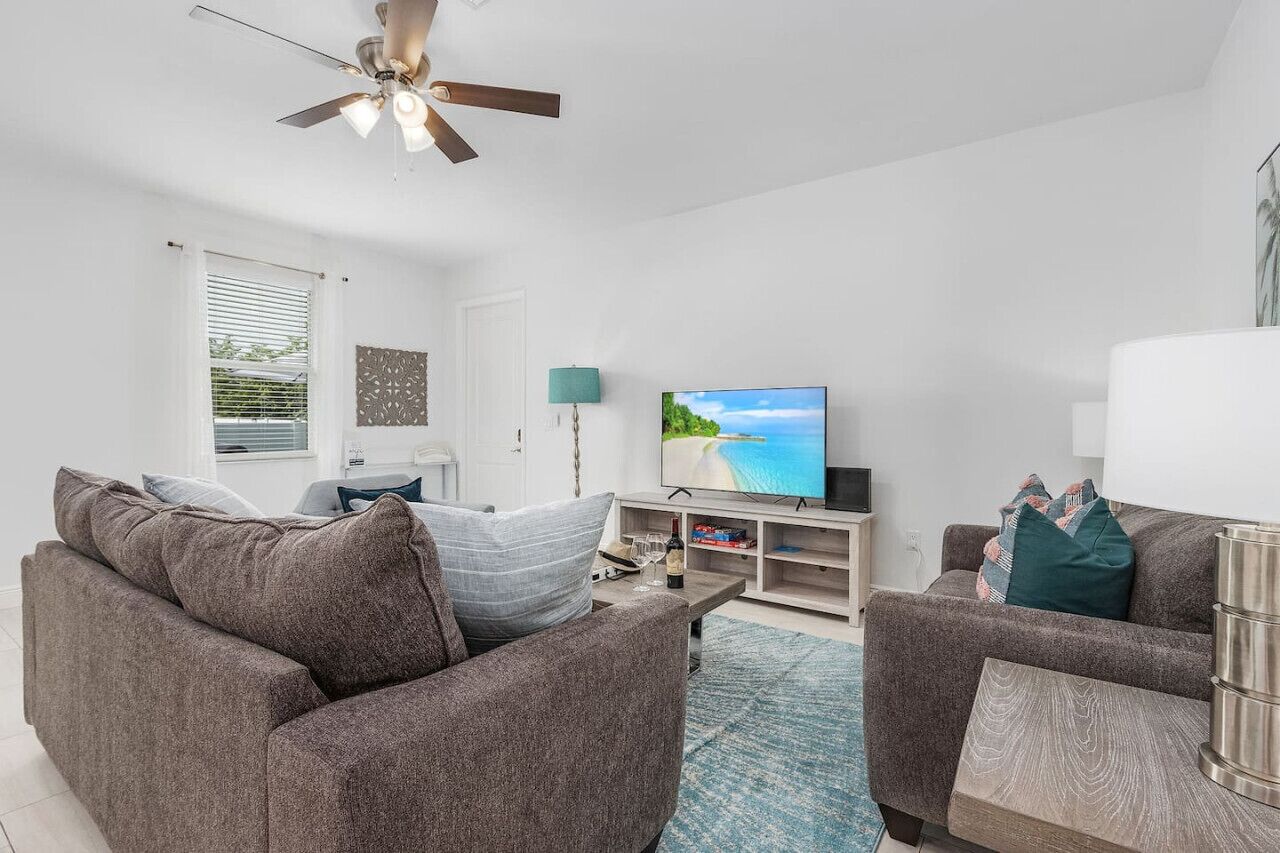 A modern living room with a flat-screen TV, two sofas, a coffee table, and a ceiling fan.