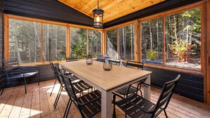 A wooden-paneled room with a large table and chairs, large windows offering a forest view, and a hanging light fixture. - Okanagan 97: Hot Tub, Pool Table & Summer Views (Les Éboulements)