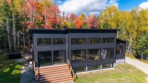 A modern two-story building with a dark exterior, large windows, and a wooden staircase leading to the entrance. - Okanagan 97: Hot Tub, Pool Table & Summer Views (Les Éboulements)