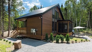 Una cabaña moderna con fachada de madera, un porche cubierto y una pequeña zona de estar al aire libre.