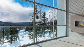 A modern interior with large windows offering a snowy mountain view. - Le Rupin 77: River, Mountain Views & Hot Tub (Charlevoix)