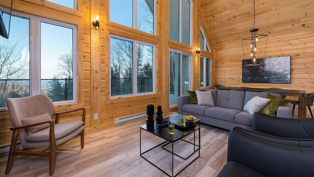 Un salón espacioso con amplias ventanas, techo de madera y muebles modernos.