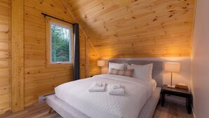 Un dormitorio de cabaña de madera con una cama, dos mesitas de noche y una ventana.