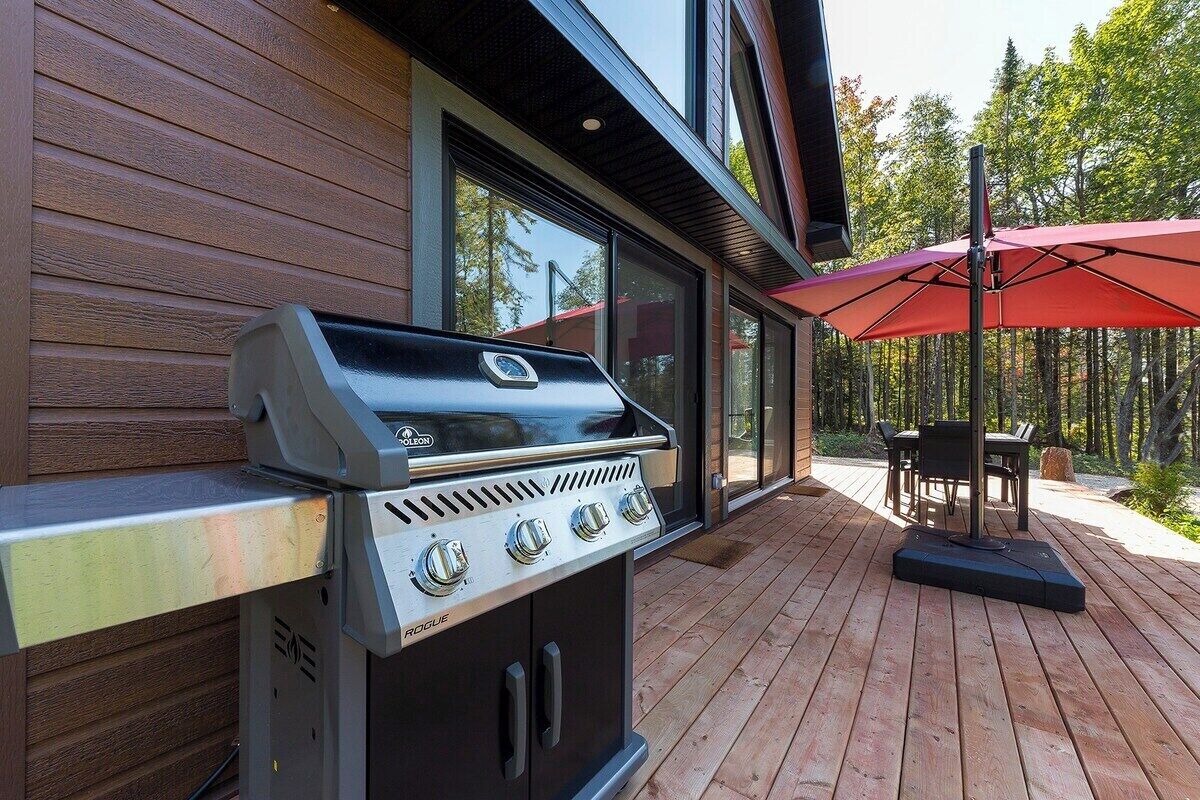 An outdoor grill area with a wooden deck, a table, and a red umbrella.