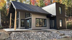 A modern two-story house with large windows and a stone foundation. - Nordik 126: Private Hot Tub, Covered Terrace & BBQ (Les Éboulements)