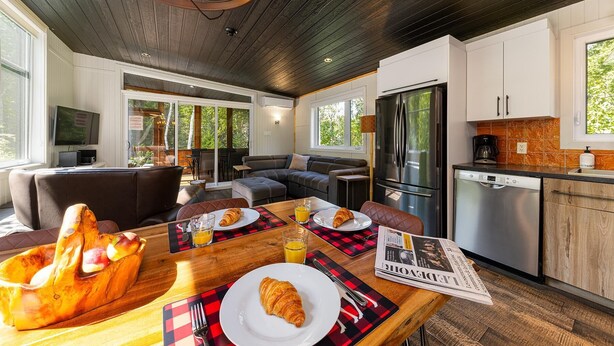Eine moderne Küche mit Kühlschrank, Herd und Kaffeemaschine. Ein Essbereich mit Tisch ist für das Frühstück gedeckt, mit Croissants und Orangensaft.