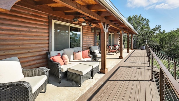 Une terrasse en bois, meublée de mobilier en osier, et une grande fenêtre donnant sur un paysage pittoresque.