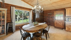 Un intérieur en bois avec une table de salle à manger ronde, des chaises, un lustre et une grande fenêtre.