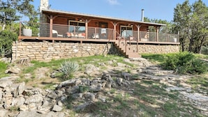 Une cabane rustique en rondins de bois, avec des fondations en pierre, une terrasse en bois et une cheminée.