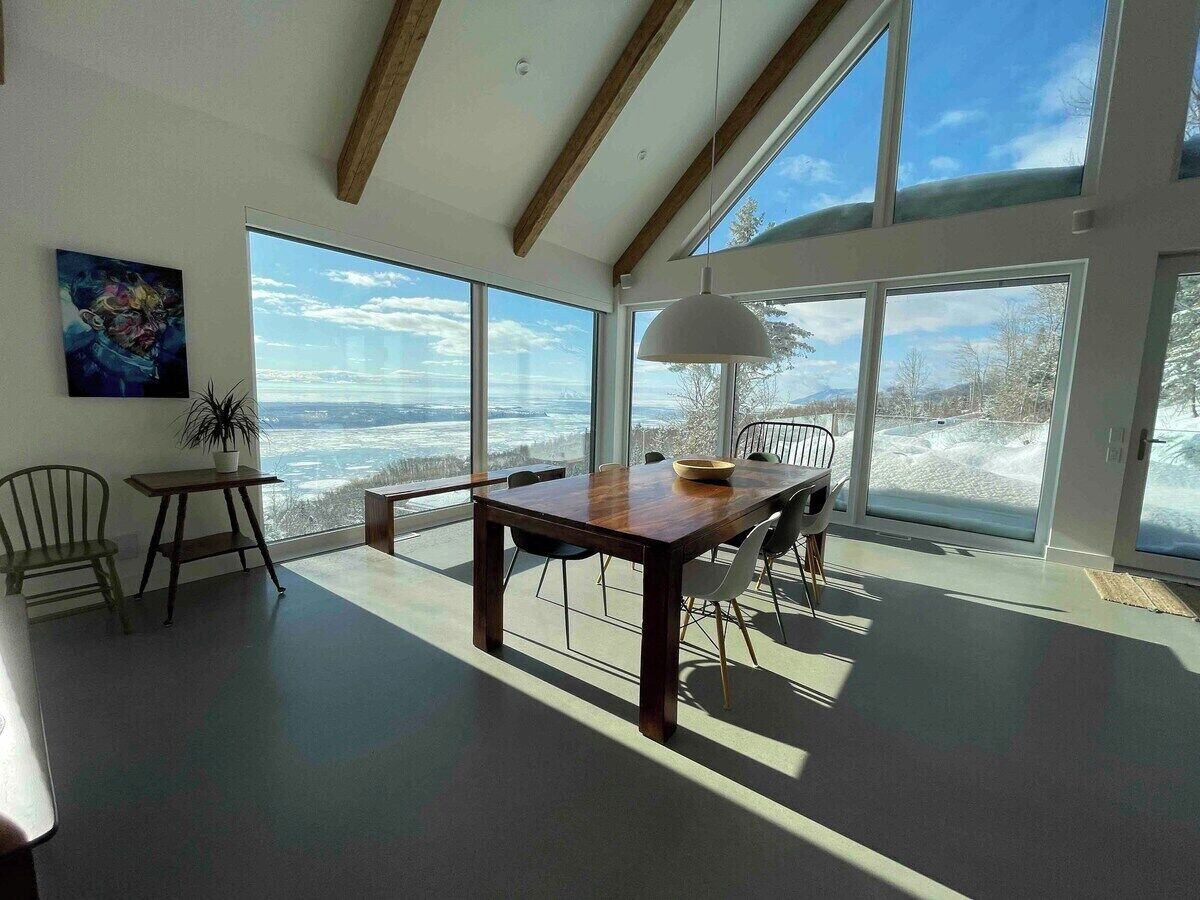 Une pièce spacieuse avec une grande table à manger, des chaises et une vue sur un paysage enneigé, visible à travers de grandes fenêtres.