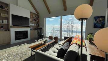 A modern living room with a large sofa, a fireplace, a TV, and a view of the outdoors.