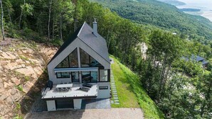 A modern house with a sloped roof, large windows, and a deck with outdoor seating.