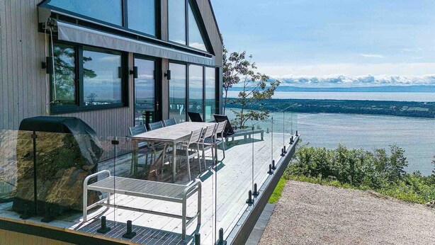 A modern house with a large glass balcony overlooking a lake.