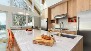 A modern kitchen with a large island, wooden cabinets, and a stainless steel refrigerator.