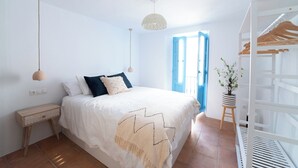 Un dormitorio con cama, mesita de noche, lámpara colgante y una puerta que da al exterior.