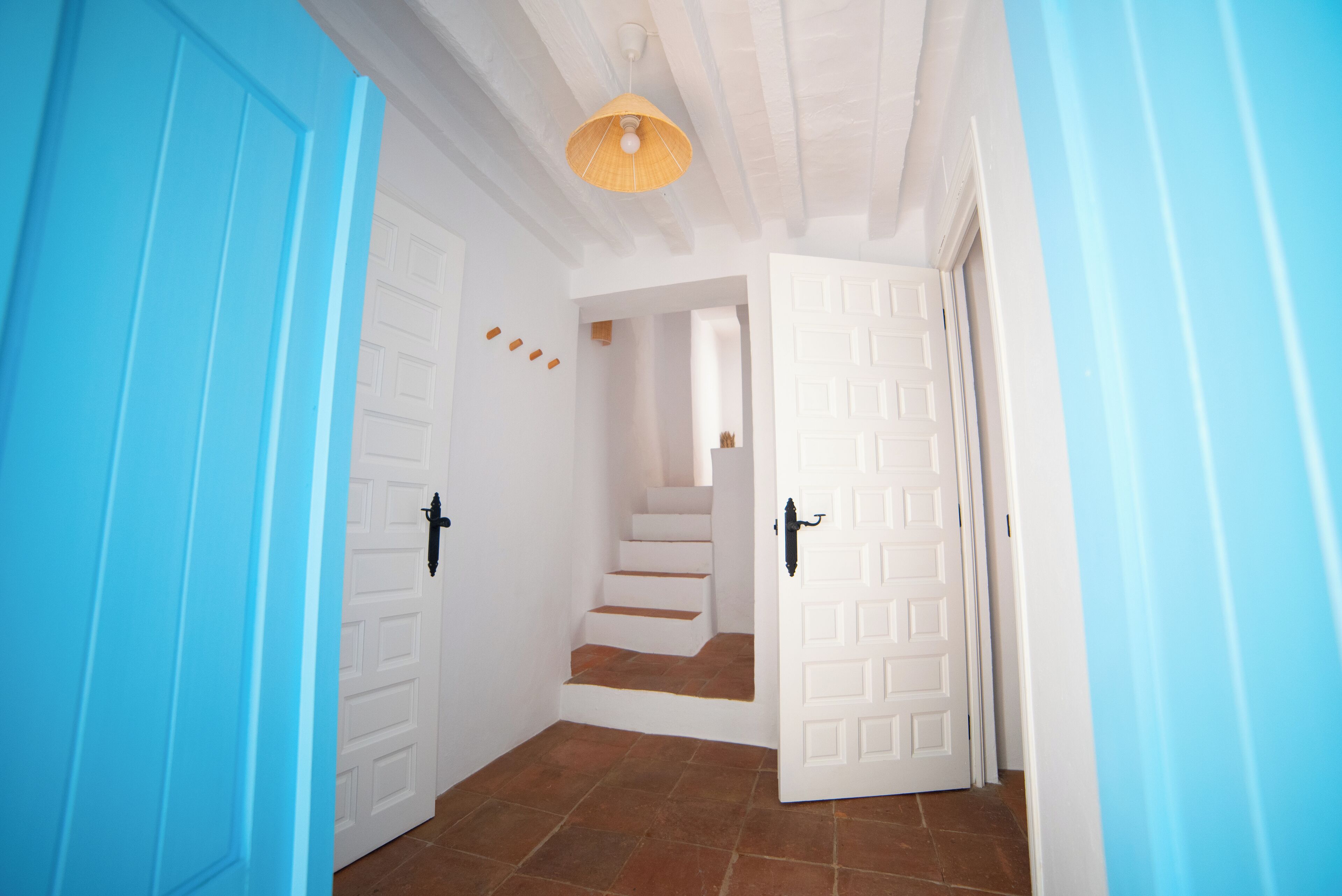 A hallway with blue doors, white walls, and a staircase leading to another room.