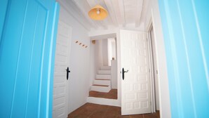 Un pasillo con puertas azules, paredes blancas y una escalera que lleva a otra habitación.