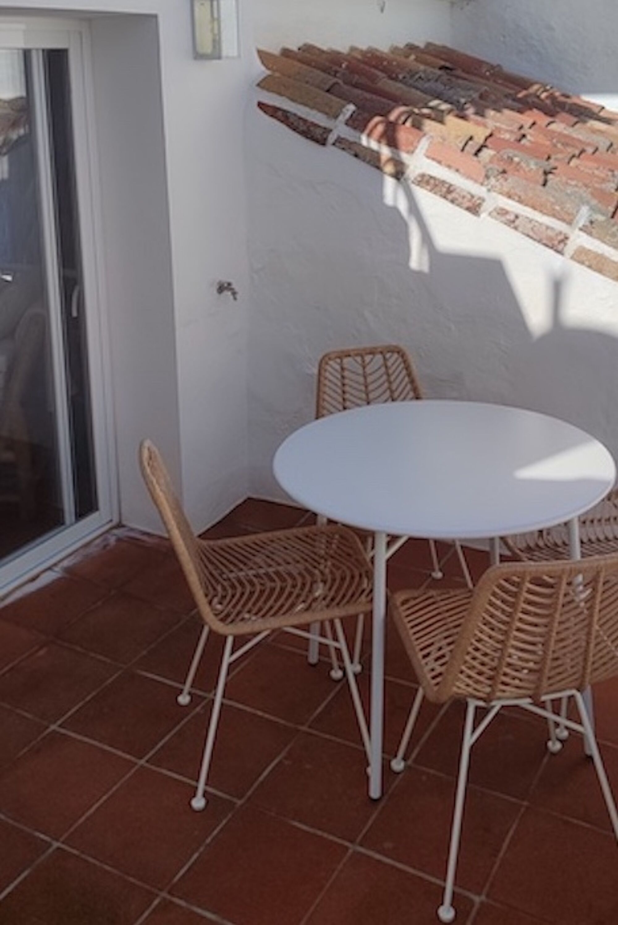 Un patio con una mesa blanca y sillas de mimbre, suelo de baldosas y pared de ladrillo.