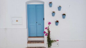 Un edificio blanco con una puerta azul, varios escalones y plantas en macetas en la pared.