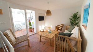 Un salón amplio con una mesa de madera, dos sillas de mimbre, una lámpara colgante tejida y una planta en maceta.