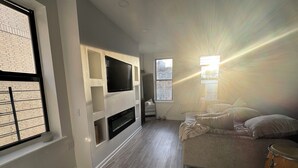 A living room with a fireplace, a flat-screen TV, a sofa, and a drum. - 3-bedroom condo in Central Park, Manhattan, Times Square!
 (New York)