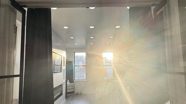 A hallway with a wooden floor, a white chair, and a window with blinds. - 3-bedroom condo in Central Park, Manhattan, Times Square!
 (New York)