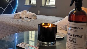 A hotel room with a bed, a remote control, a candle, and a bottle of linen spray on a glass table. - 3-bedroom condo in Central Park, Manhattan, Times Square!
 (New York)