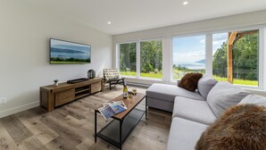 A modern living room with a large window, a sofa, a coffee table, and a TV mounted on the wall.