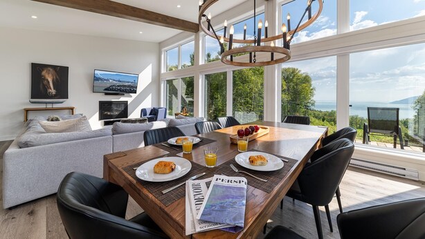 A modern dining area with a wooden table, black chairs, and a view of the outdoors.