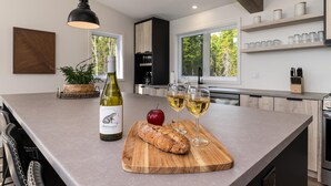 A modern kitchen with a large island, wine bottle, glasses, and a loaf of bread.