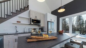 Une cuisine moderne dotée d’un îlot central, d’appareils électroménagers en acier inoxydable et d’une grande fenêtre offrant une vue sur les arbres.