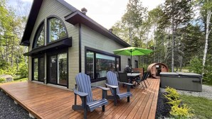 Une maison moderne dotée d’une terrasse, de deux fauteuils Adirondack, d’une table et d’un barbecue.
