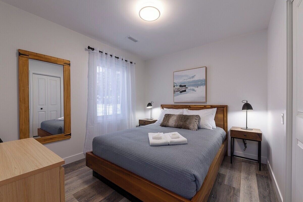 A bedroom with a wooden bed, a bedside table with a lamp, a mirror, and a painting on the wall.