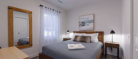 A bedroom with a wooden bed, a bedside table with a lamp, a mirror, and a painting on the wall.