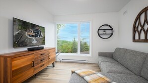 Un salon moderne doté d’une grande fenêtre, d’un meuble en bois, d’un canapé gris et d’un téléviseur à écran plat fixé au mur.