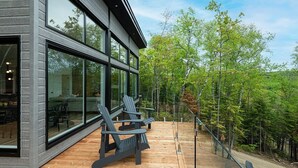 Un bâtiment moderne doté de grandes fenêtres et d’une terrasse aménagée avec des fauteuils Adirondack.