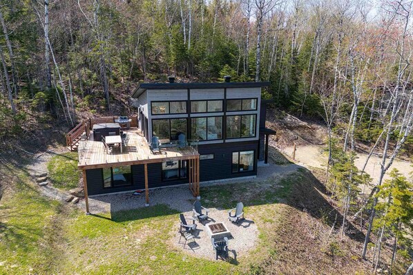 Une maison moderne à deux étages, dotée d’une terrasse et entourée d’une forêt.