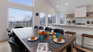 A modern dining area with a large table set for breakfast, including croissants, fruit, and juice. - Le Chaleureux 61: River & Mountain Views (Petite-Rivière-Saint-François)