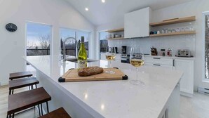 A modern kitchen with a large island, white cabinetry, and a view of the outdoors. - Le Chaleureux 61: River & Mountain Views (Petite-Rivière-Saint-François)