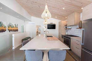 Een moderne keuken met een centraal kookeiland, houten plafond en een hanglamp.