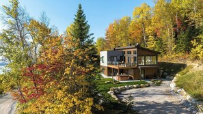 Een modern huis met balkon, omgeven door herfstkleurige bladeren en een heldere lucht.
