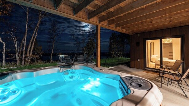 A hot tub in an outdoor wooden deck area with a view of the night sky and trees. - Chez Annie 215: Panoramic Views & Hot Tub (Charlevoix)