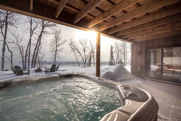 Een jacuzzi met uitzicht op een besneeuwd landschap en kale bomen.