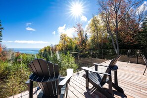 A deck with Adirondack chairs overlooking a scenic view of a body of water and autumn foliage. - Refuge 2: Hot Tub, River Views & Pet Friendly (Les Éboulements)